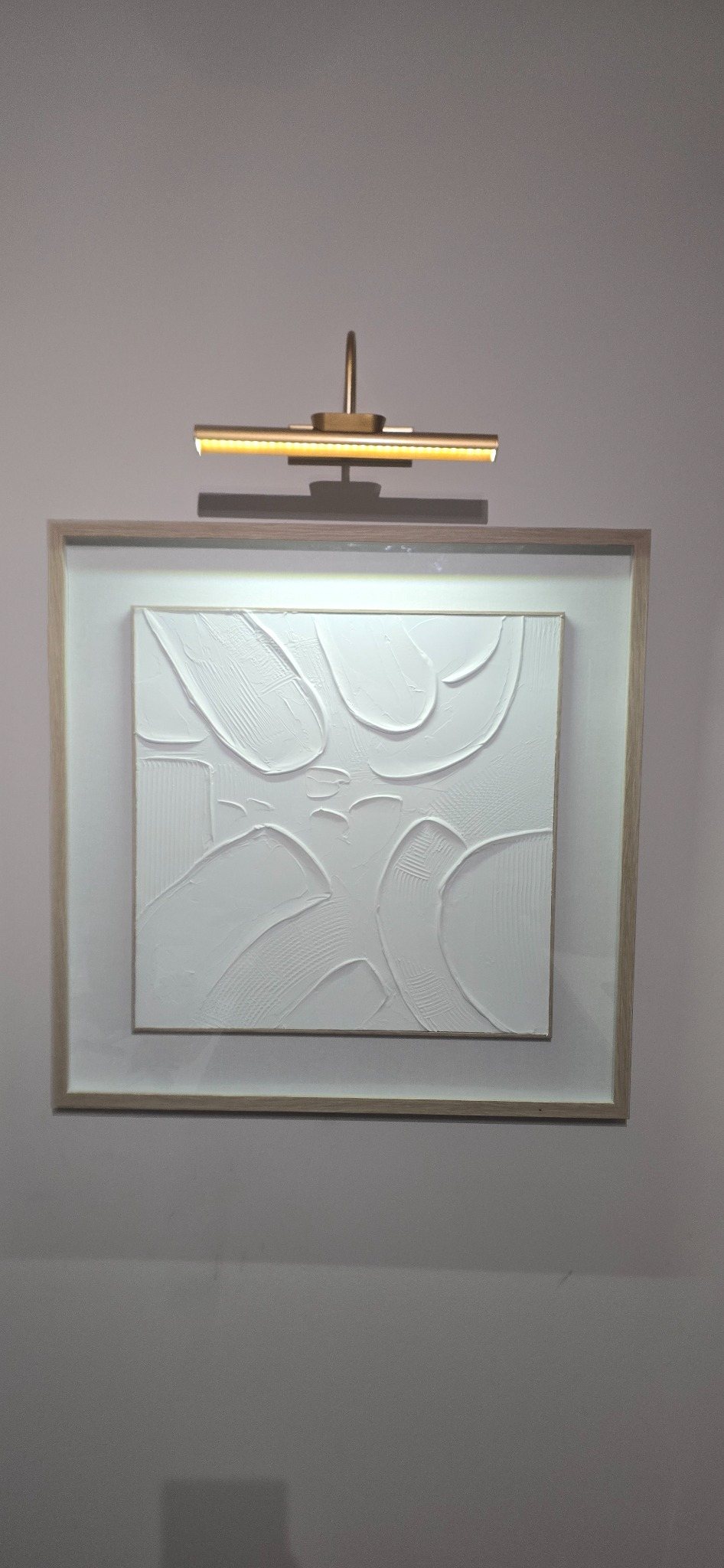 Framed white textured artwork aligned beneath a picture light